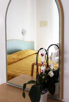 Specchio riflette letto con copriletto giallo e orchidea in vaso.