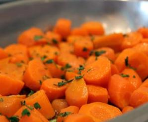 Carote cotte a fette, guarnite con erbe aromatiche in una ciotola di metallo.