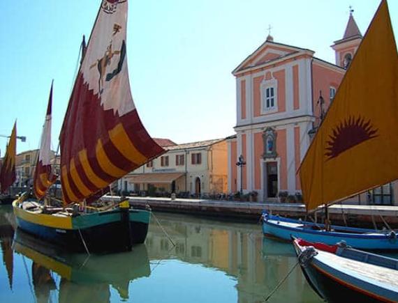 Barche a vela storiche in un canale con una chiesa sullo sfondo.