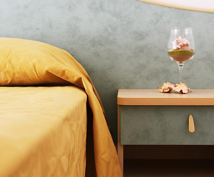 Letto con copriletto giallo, comodino con bicchiere decorativo e conchiglie.