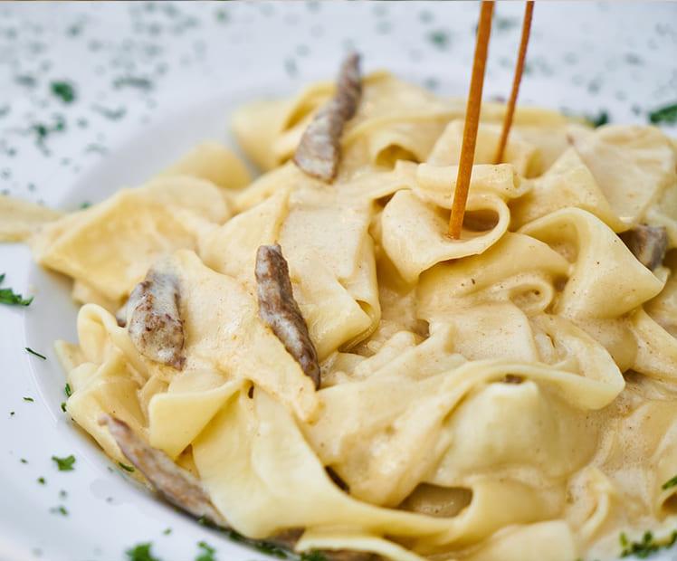 Tagliatelle alla panna con funghi su piatto bianco, decorato con prezzemolo.